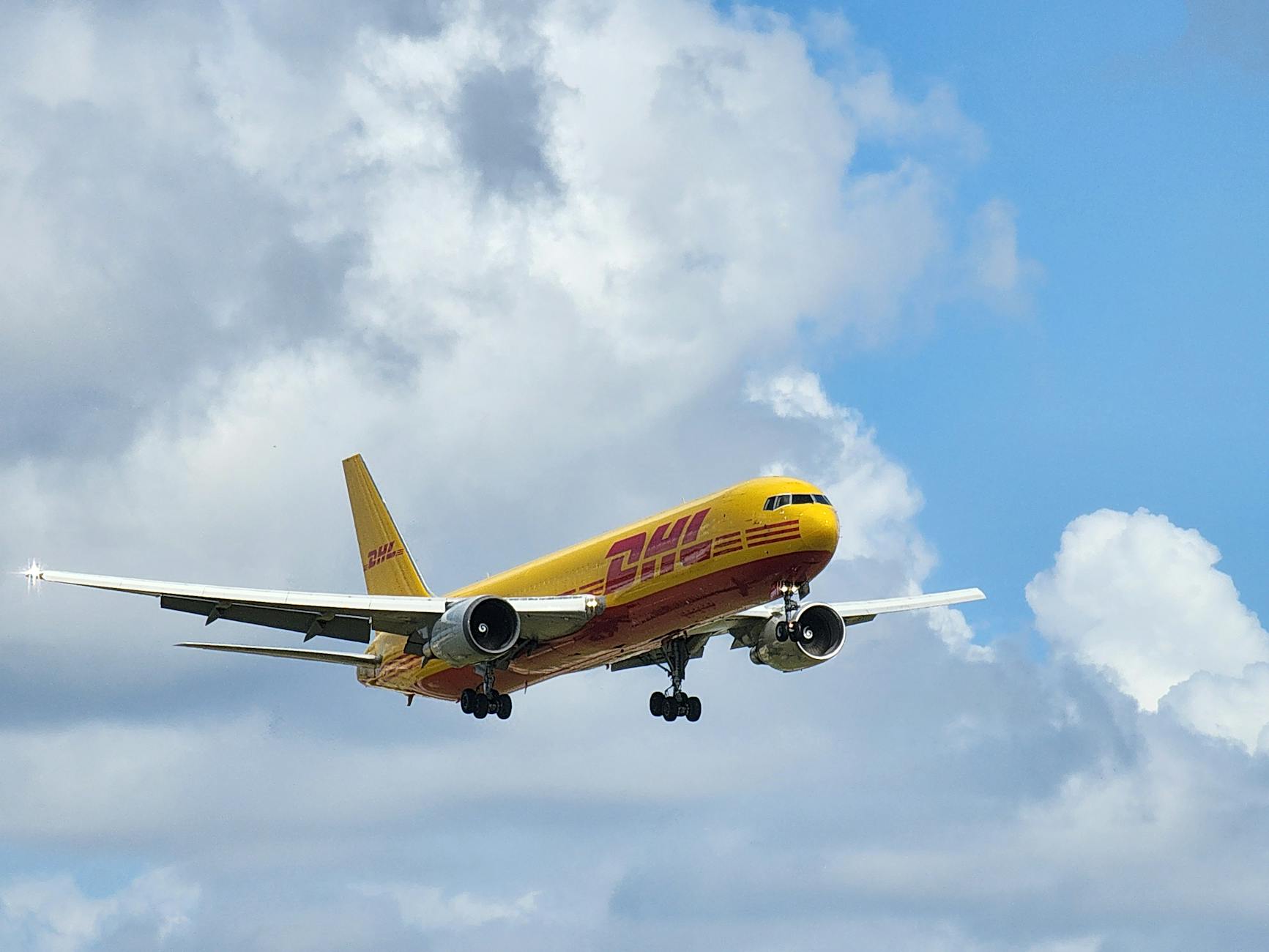 DHL cargo plane flying against bright blue sky with clouds